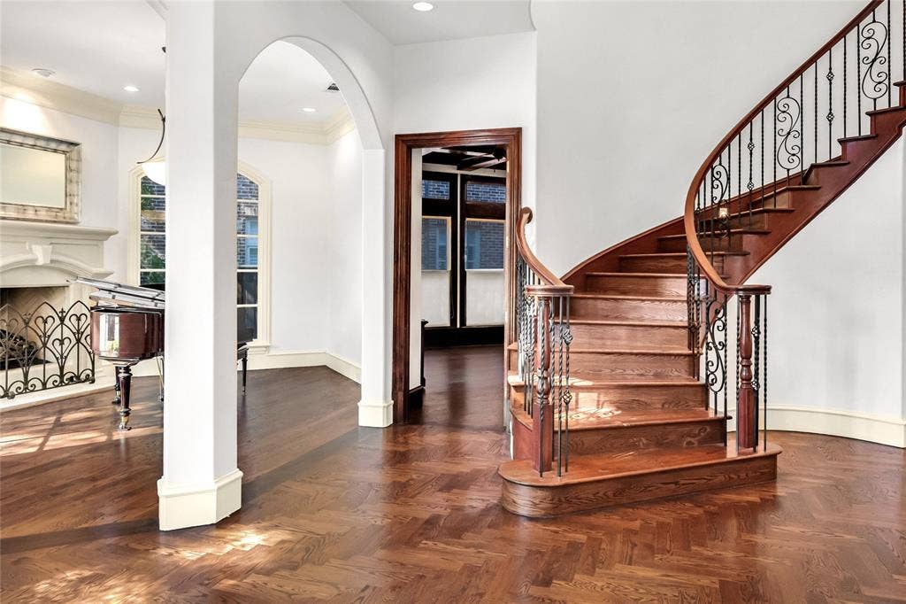 Foyer featuring herringbone wood-finish flooring, a curved staircase with ornate iron balusters, an arched architectural opening, and a decorative fireplace mantel