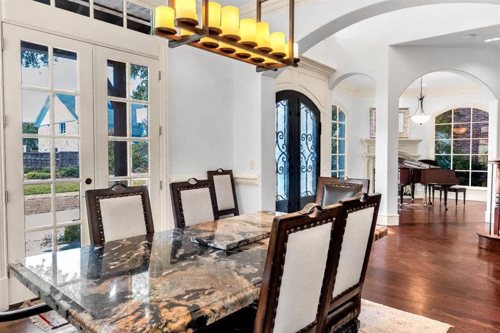 Dining area featuring wood-finish flooring, multi-pane glass French doors, arched architectural openings, an iron-accented chandelier, and ornate wrought-iron door inserts