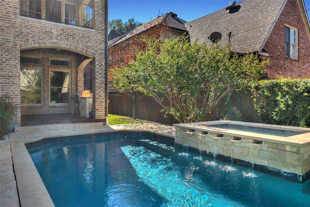 Backyard featuring a custom swimming pool, raised spa with stone masonry, integrated water features, and a covered patio with a built-in outdoor grill