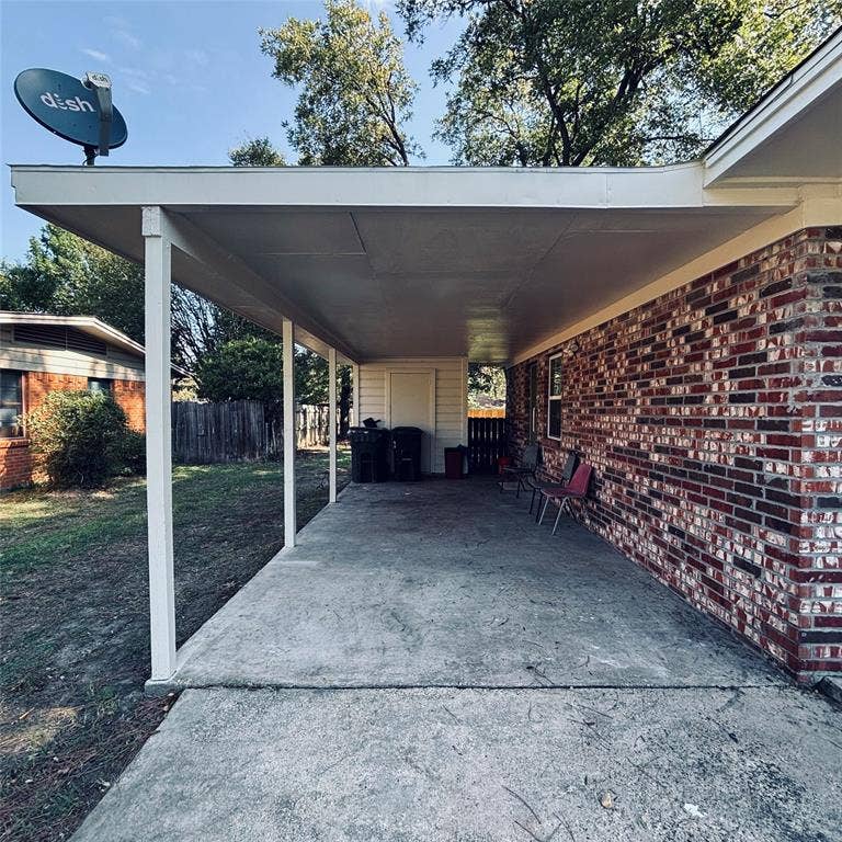 Covered carport featuring a concrete floor, brick exterior wall, and attached utility storage closet