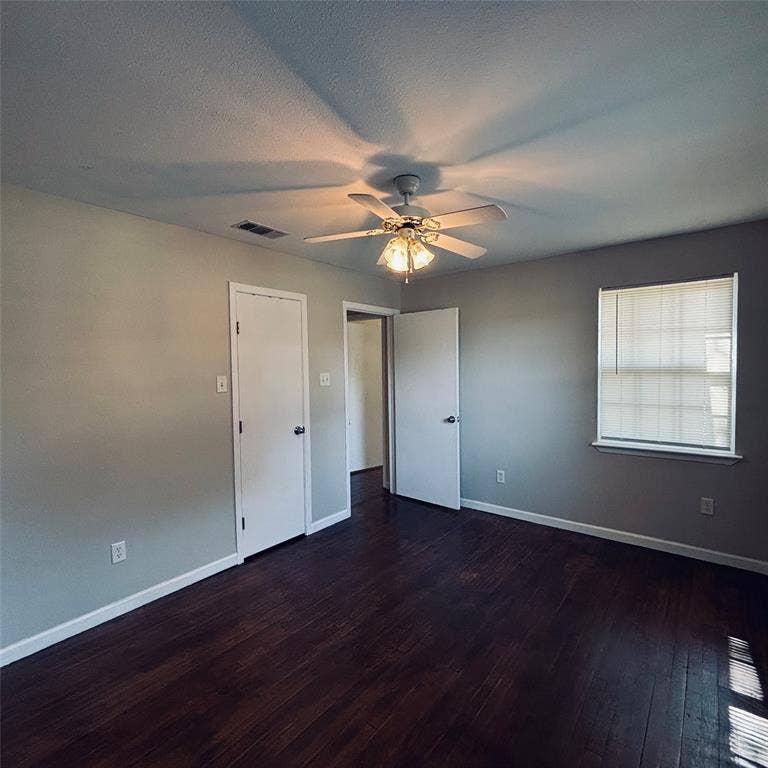 Room featuring dark wood-finish flooring, a neutral wall palette, a multi-light ceiling fan, and a window with fitted blinds
