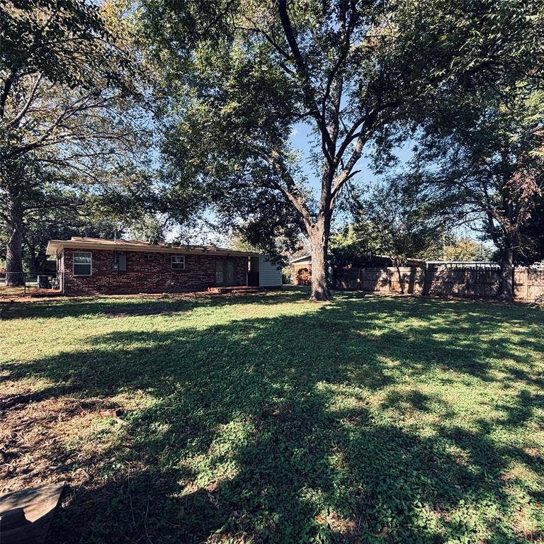 Expansive backyard featuring a brick exterior, mature trees, and a wooden privacy fence