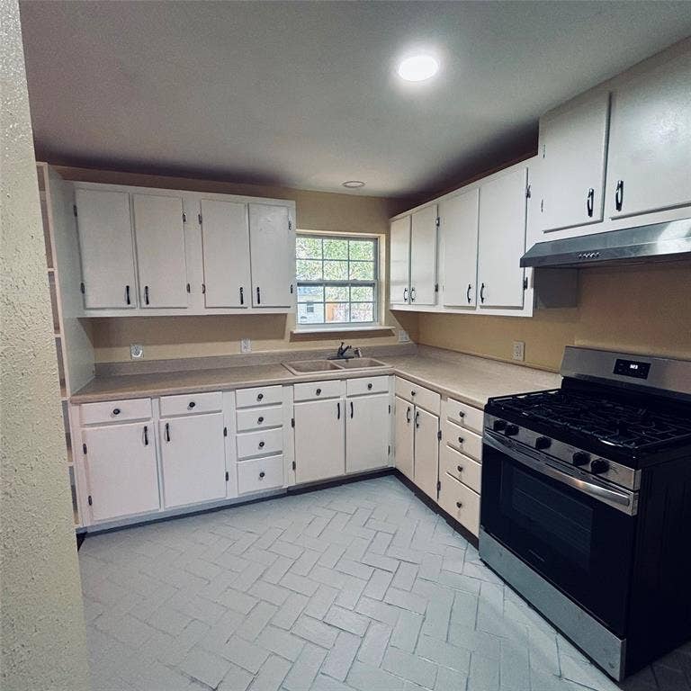 Kitchen featuring white cabinetry, solid-surface countertops, dual-basin sink, integrated stainless steel range hood, and herringbone-patterned tile flooring