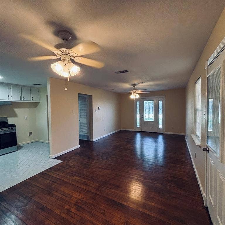 Interior featuring wood-finish flooring, dual ceiling fans with integrated lighting, white kitchen cabinetry, and an exterior door with glass panes