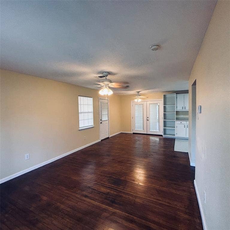 Wood-finish flooring, dual ceiling fans with light kits, built-in floor-to-ceiling cabinetry, and glass-paneled double doors