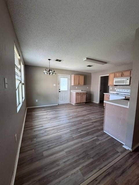Open-concept space featuring wood-finish flooring, light wood cabinetry, white built-in appliances, and a multi-arm pendant light fixture