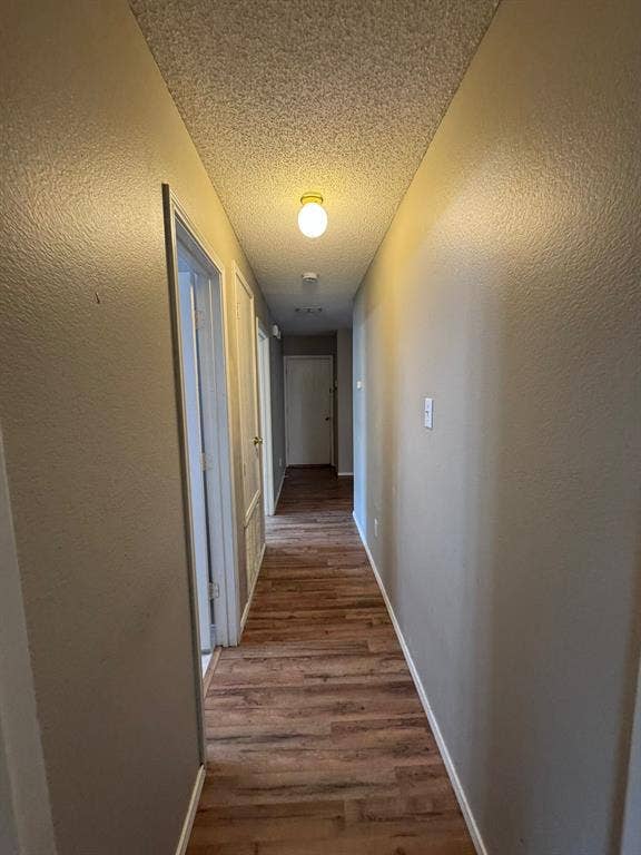 Hallway featuring wood-finish flooring, textured ceilings, and flush-mount light fixtures