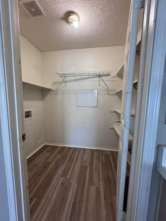 Storage space featuring wood-finish flooring, integrated wire shelving, fixed wall shelving, and utility hookups