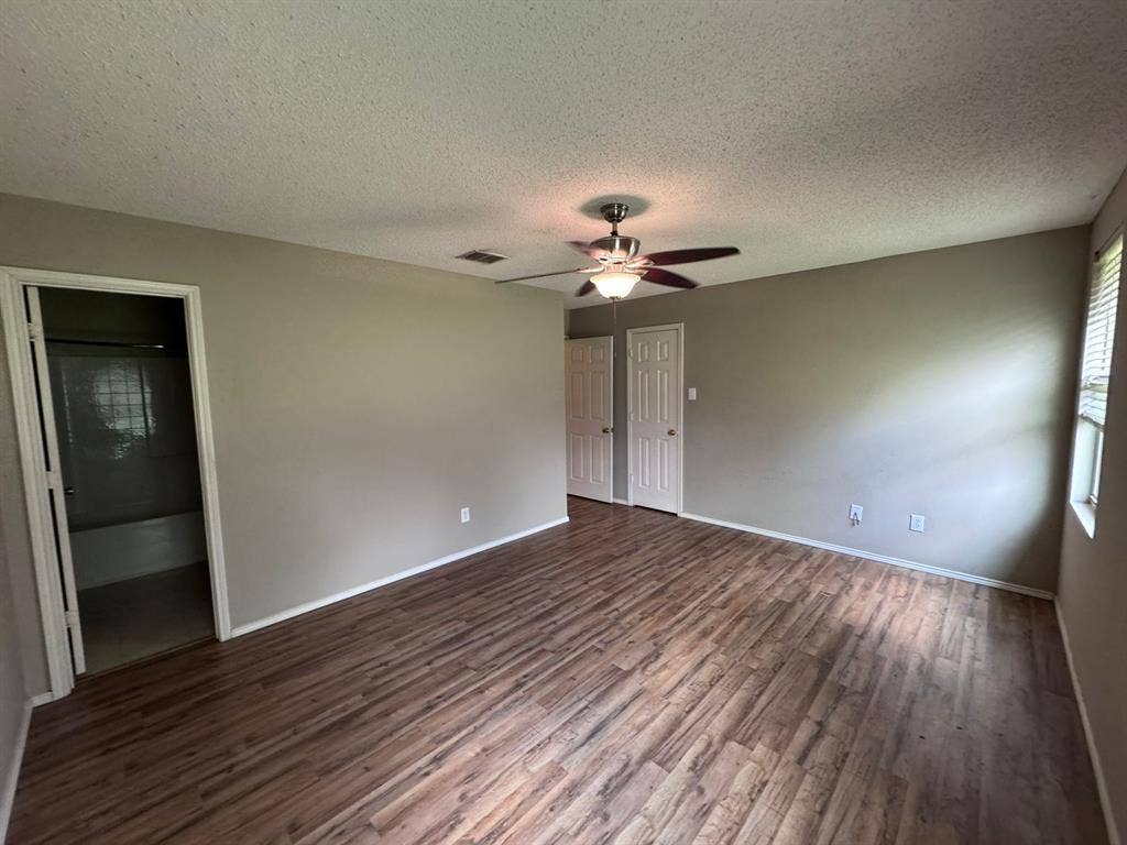 Wood-finish flooring, ceiling fan with integrated lighting, textured ceiling, and paneled doors