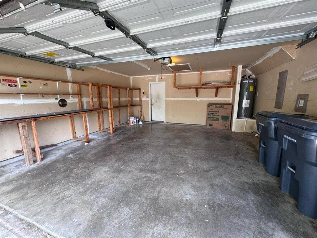 Two-car garage featuring a concrete floor, built-in wooden wall shelving, and an integrated water heater