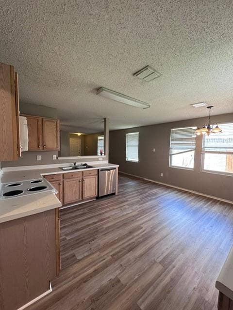 Kitchen featuring wood-finish cabinetry, solid surface countertops, a stainless steel dishwasher, and wood-finish flooring throughout the space
