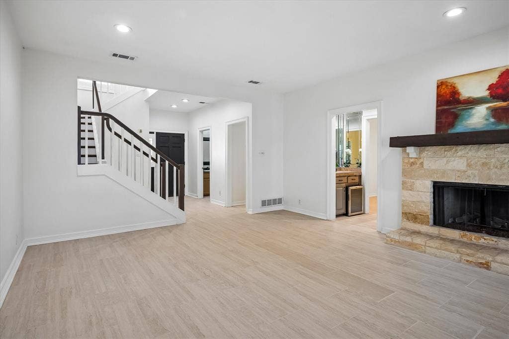4611 O Connor Court, Irving, TX 75062 Open-concept living space featuring wood-finish flooring, recessed lighting, a floor-to-ceiling stone fireplace with a substantial timber mantel, and a staircase with white balusters and a dark wood handrail