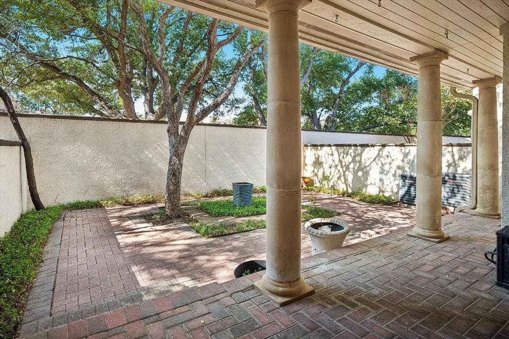4611 O Connor Court, Irving, TX 75062 Covered brick patio featuring structural stone columns, perimeter stucco wall, herringbone brick pavers, and mature trees