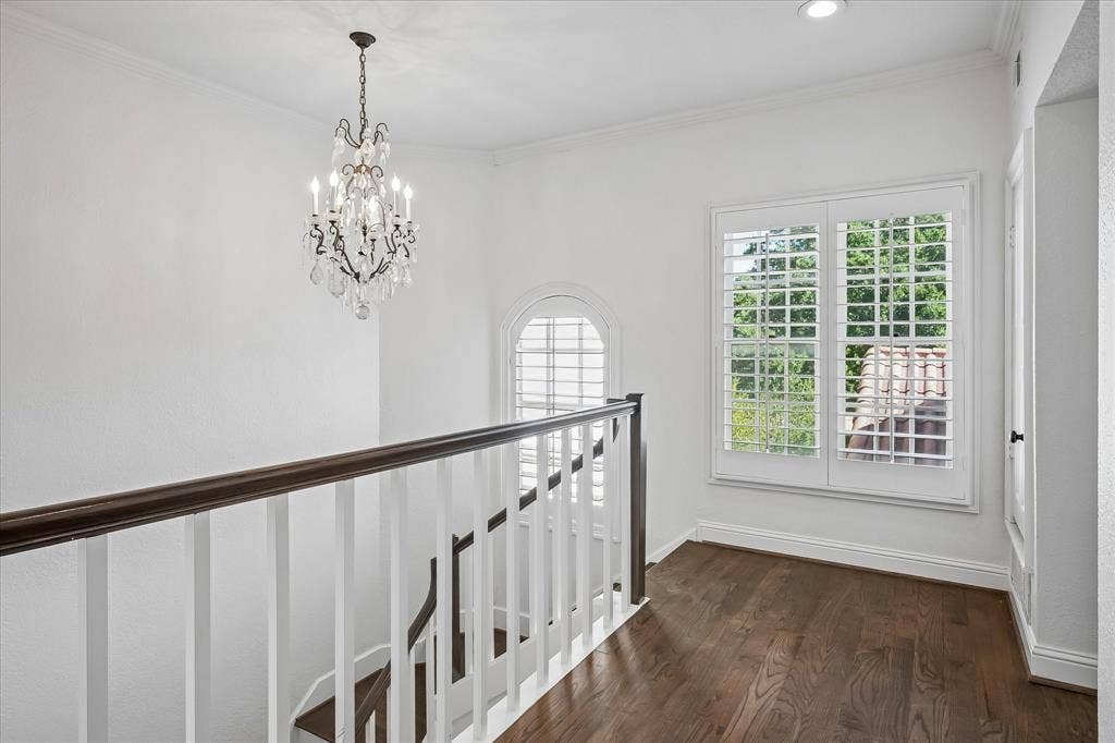 4611 O Connor Court, Irving, TX 75062 Landing area featuring wood-finish flooring, a tiered crystal chandelier, white balustrades with a dark wood handrail, arched windows, and white plantation shutters