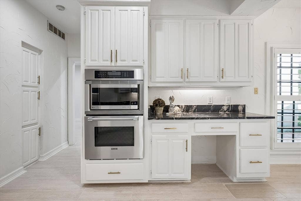 4611 O Connor Court, Irving, TX 75062 Kitchen cabinetry featuring white shaker-style doors, brass-finish hardware, dark stone-finish countertops, stainless steel built-in double ovens, and a dedicated workspace area