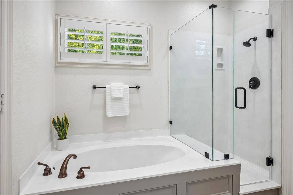 4611 O Connor Court, Irving, TX 75062 Oversized soaking tub with solid-surface surround, walk-in shower with frameless glass enclosure, matte black plumbing fixtures, and white plantation shutters