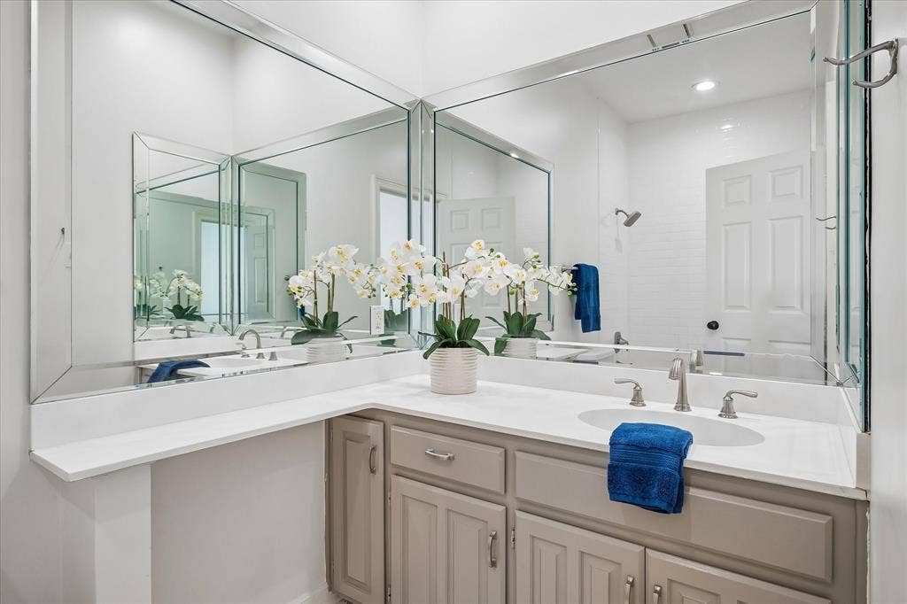 4611 O Connor Court, Irving, TX 75062 L-shaped vanity featuring light-toned cabinetry, solid surface countertop, undermount sink, widespread faucet, and expansive wall-to-wall beveled mirrors