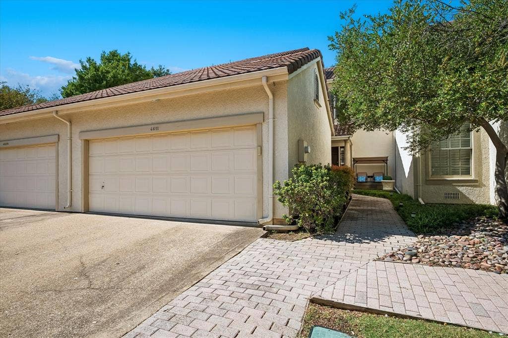 4611 O Connor Court, Irving, TX 75062 Stucco exterior featuring a two-car garage with paneled doors, a tiled roof, and a paver walkway