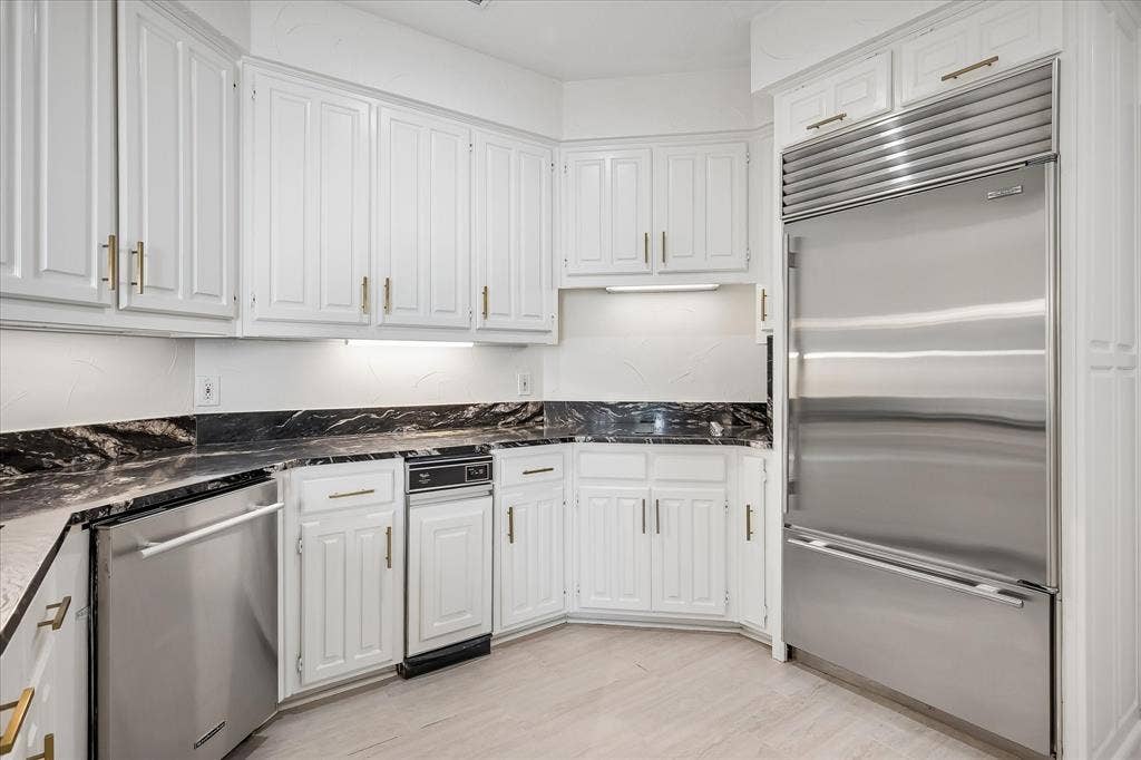 4611 O Connor Court, Irving, TX 75062 Kitchen featuring white raised-panel cabinetry with brass-finish hardware, dark stone-patterned countertops, stainless steel integrated refrigerator, built-in dishwasher, and wood-finish flooring