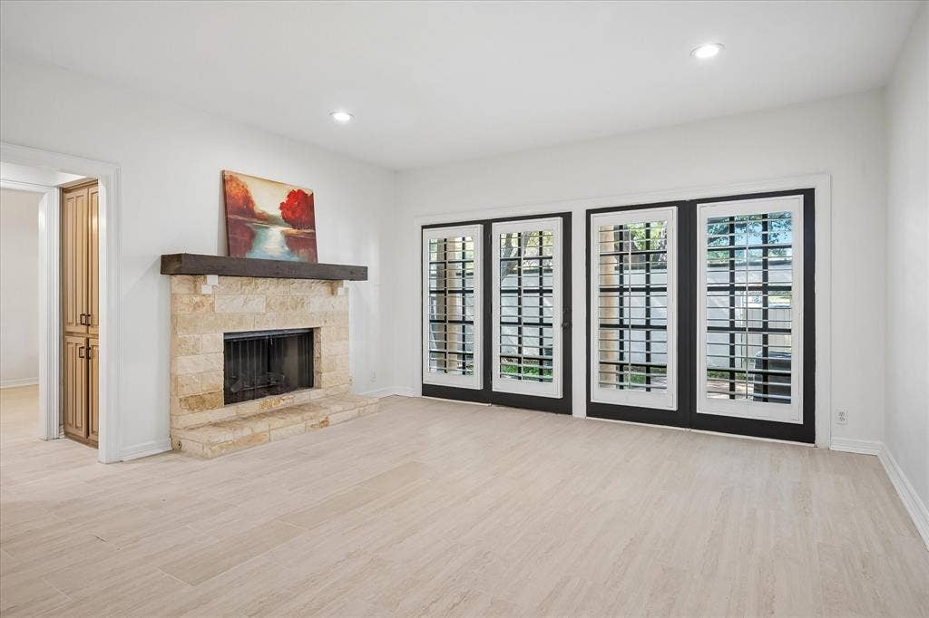 4611 O Connor Court, Irving, TX 75062 Stone fireplace with a prominent timber mantel, light-toned wood-finish flooring, and multiple sets of glass-paneled doors with black frames
