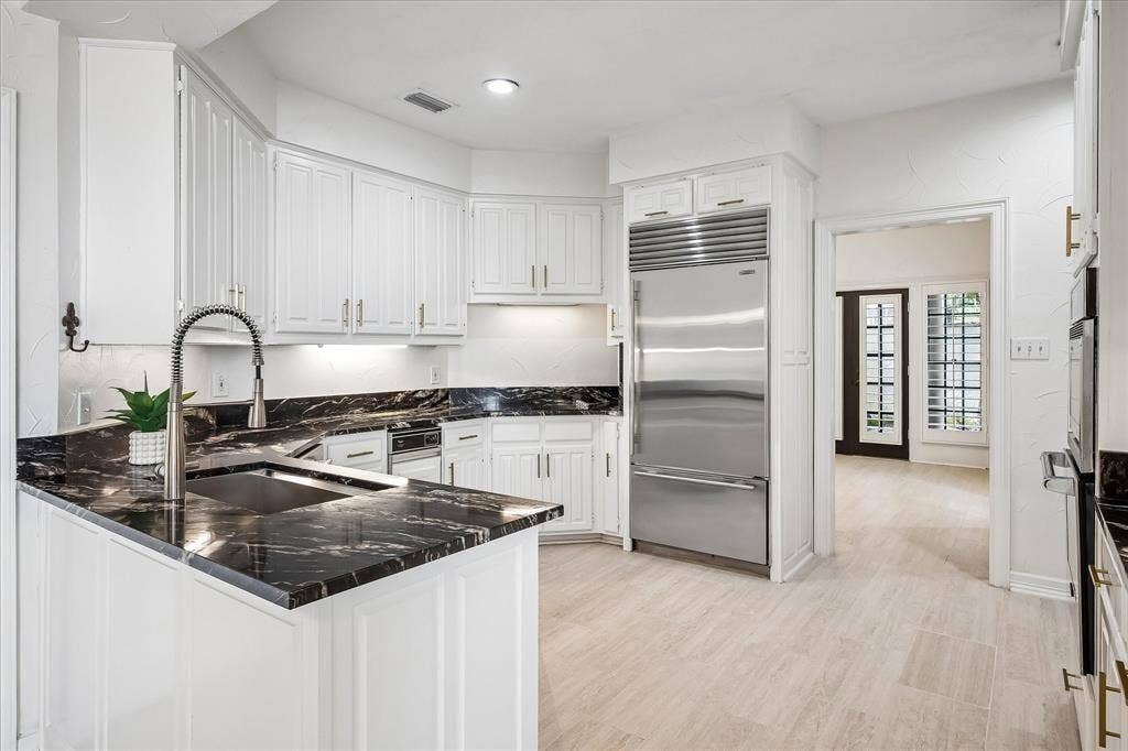 4611 O Connor Court, Irving, TX 75062 Kitchen featuring white cabinetry, dark stone countertops, integrated stainless steel refrigerator, undermount sink with pull-down faucet, and light-tone flooring