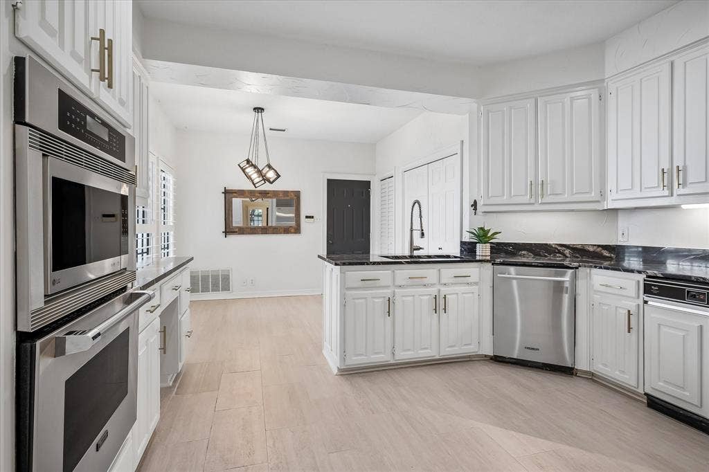 4611 O Connor Court, Irving, TX 75062 Kitchen featuring white cabinetry with gold-tone hardware, dark stone countertops, stainless steel wall-mounted oven and microwave, and light-toned wood-finish flooring