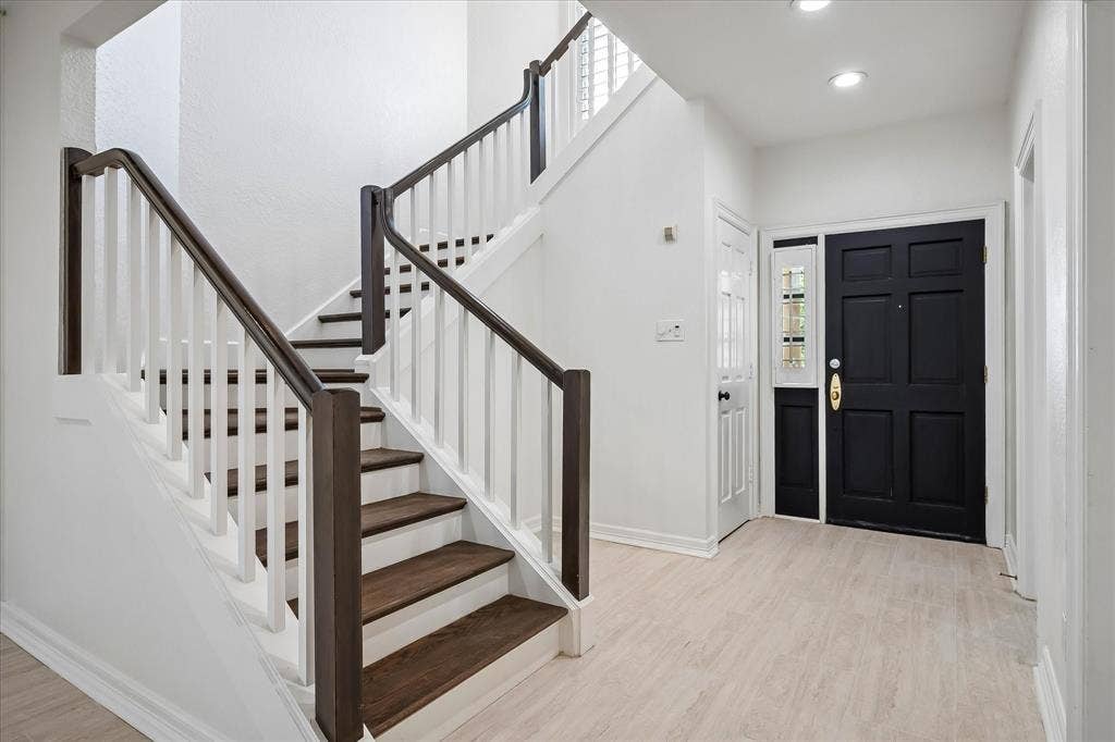 4611 O Connor Court, Irving, TX 75062 Foyer featuring a black paneled front door with a glass sidelight, wood-finish flooring, and a staircase with white balusters and dark-stained handrails and treads