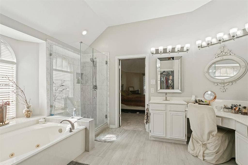 3212 Chippenham Drive, Plano, TX 75093 Bathroom featuring a jetted soaking tub, glass-enclosed shower with tiled surround, dual-mirrored vanity area with built-in cabinetry, and wood-finish flooring