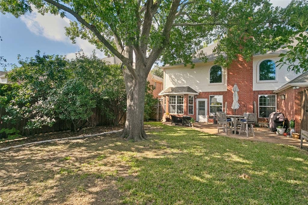 3212 Chippenham Drive, Plano, TX 75093 Brick Colonial home with expansive rear grounds featuring mature shade trees, manicured lawn, and covered patio with outdoor seating area