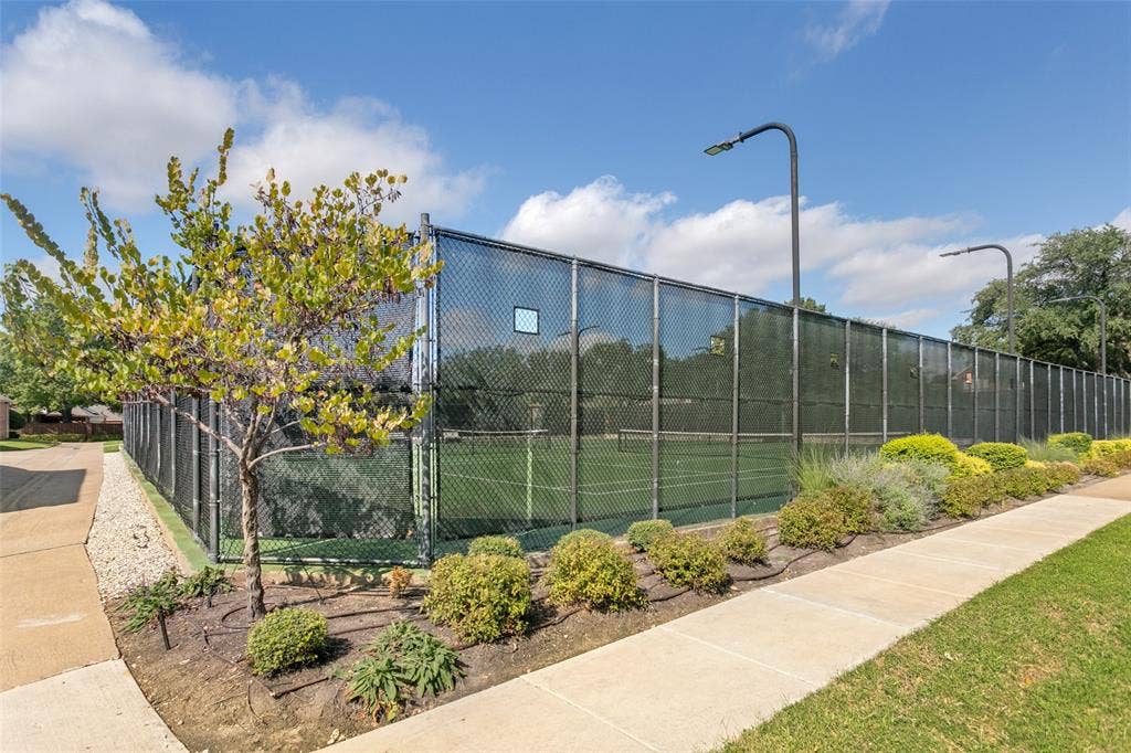 3212 Chippenham Drive, Plano, TX 75093 Private tennis court enclosed by chain-link fencing, featuring integrated pole-mounted lighting, concrete walkways, and landscaped shrubbery