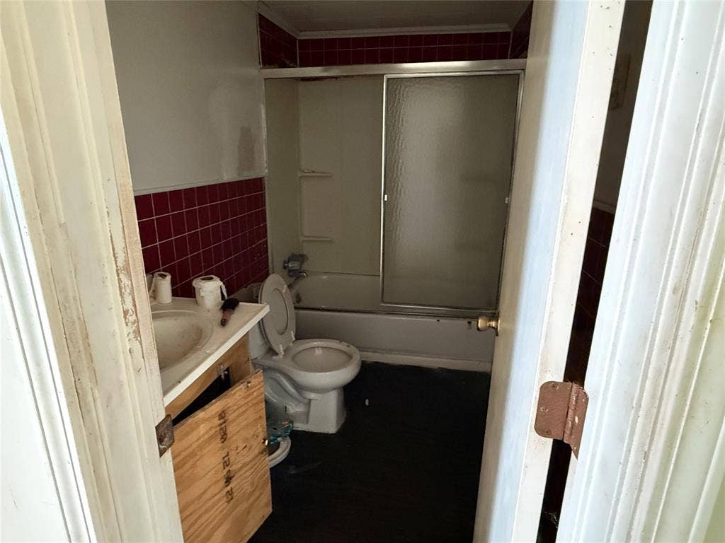 Bathroom featuring a shower and tub combination with a sliding glass enclosure, crimson-tiled wall surrounds, and a vanity cabinet