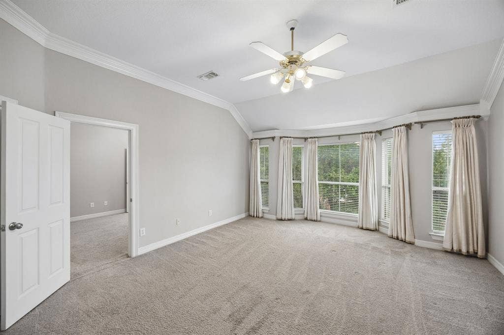 Vaulted ceilings, bay window configuration, neutral carpeting, ceiling fan with integrated lighting, and multi-panel interior door