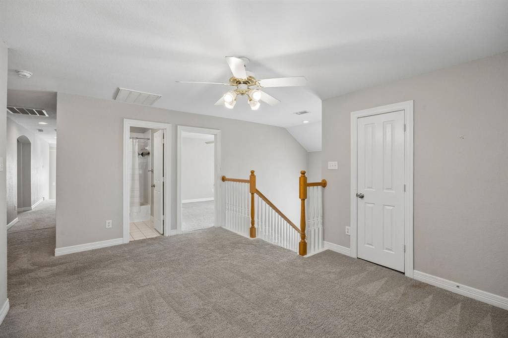 Neutral-toned carpeting, ceiling fan with integrated light fixture, and wooden staircase railing featuring white balusters