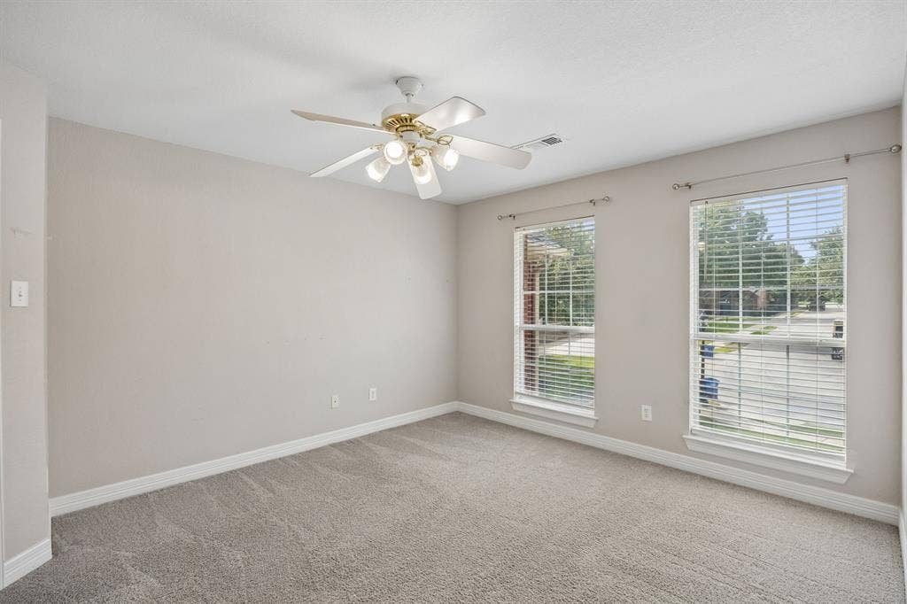 Neutral-toned interior space featuring neutral wall-to-wall carpeting, two dual-pane windows with horizontal blinds, and a white ceiling fan with integrated multi-bulb lighting