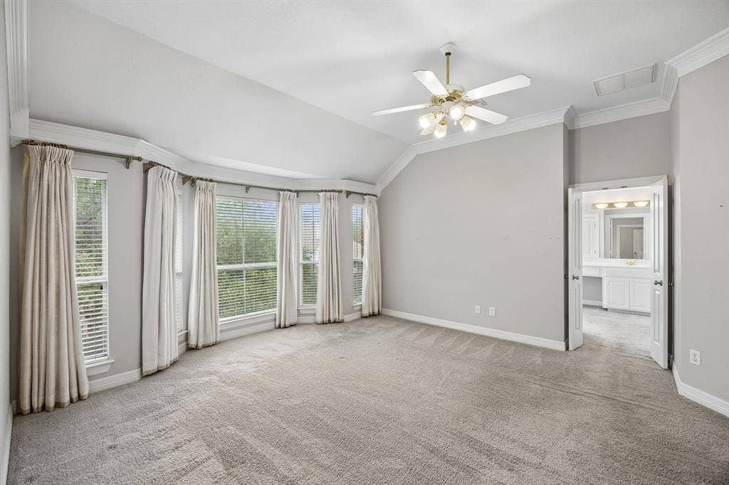 Vaulted ceilings, bay window configuration, neutral wall finishes, carpeted flooring, and a multi-light ceiling fan