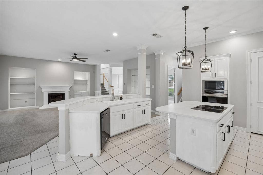 Kitchen featuring white cabinetry, an island with an integrated cooktop, stone-surfaced countertops, built-in dual ovens, and geometric pendant lighting