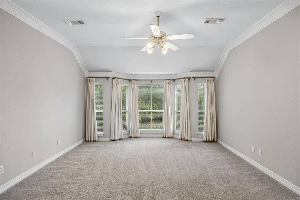 Vaulted ceilings, expansive bay window, ceiling fan with integrated lighting, and neutral carpeting