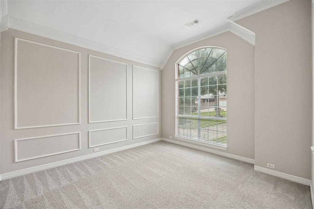 Room featuring vaulted ceilings, arched window with a grid pattern, and walls finished with decorative crown molding and wainscoting panels
