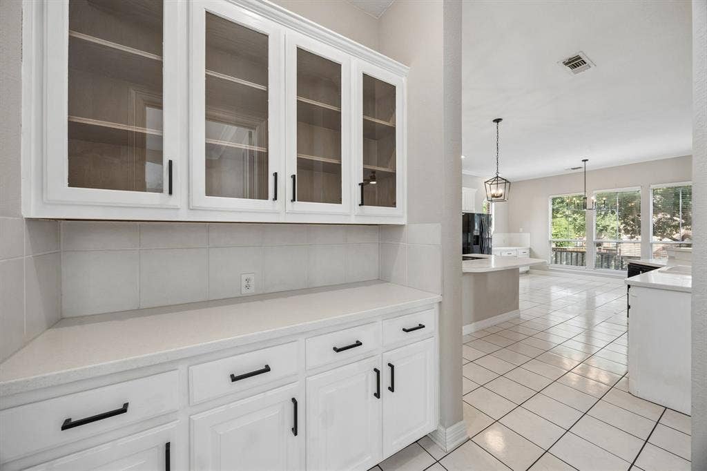 White cabinetry with glass-front upper doors, stone-finish countertops, matte black hardware, square tile backsplash, and ceramic tile flooring