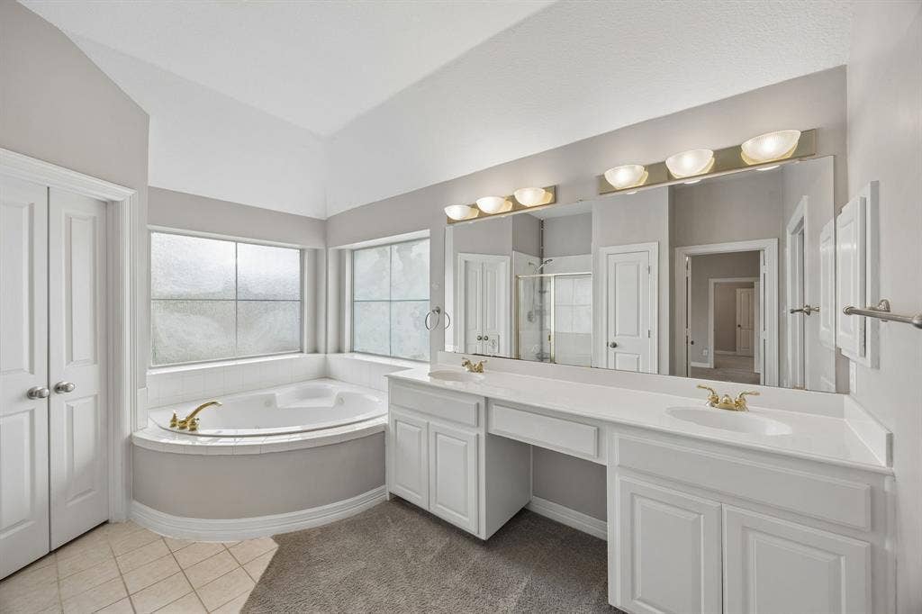 Dual-vanity cabinetry with white finish, integrated countertop with dual sinks, corner soaking tub, large vanity mirror, and multi-light wall fixtures