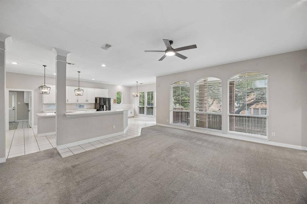 Open-concept interior featuring arched windows, white cabinetry with breakfast bar, neutral carpeting, and a ceiling-mounted fan with integrated light