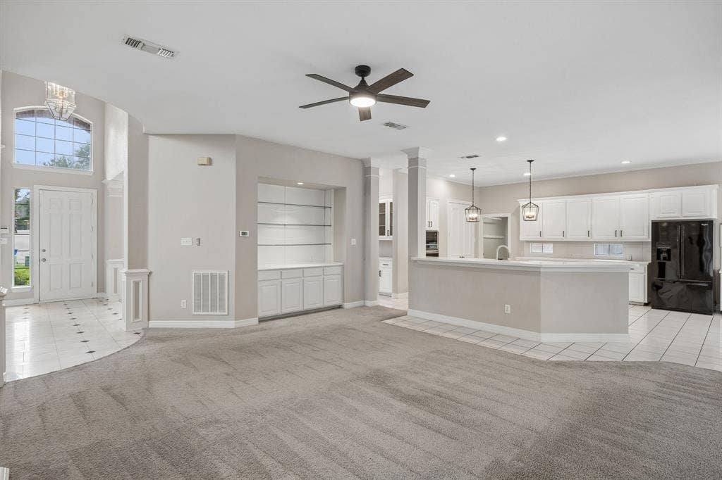 Open-concept interior featuring a breakfast bar, white cabinetry, built-in display shelving, tile flooring, and vaulted ceilings