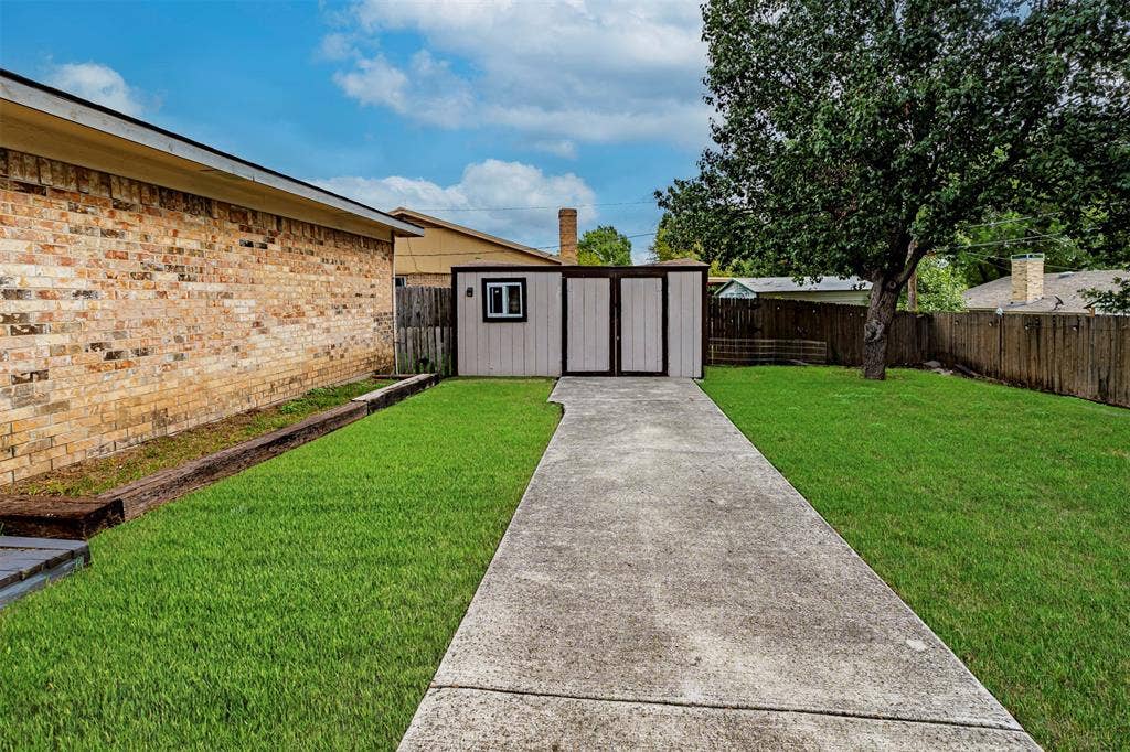 Backyard featuring a concrete walkway, detached storage structure, brick exterior wall, and wood-paneled fencing