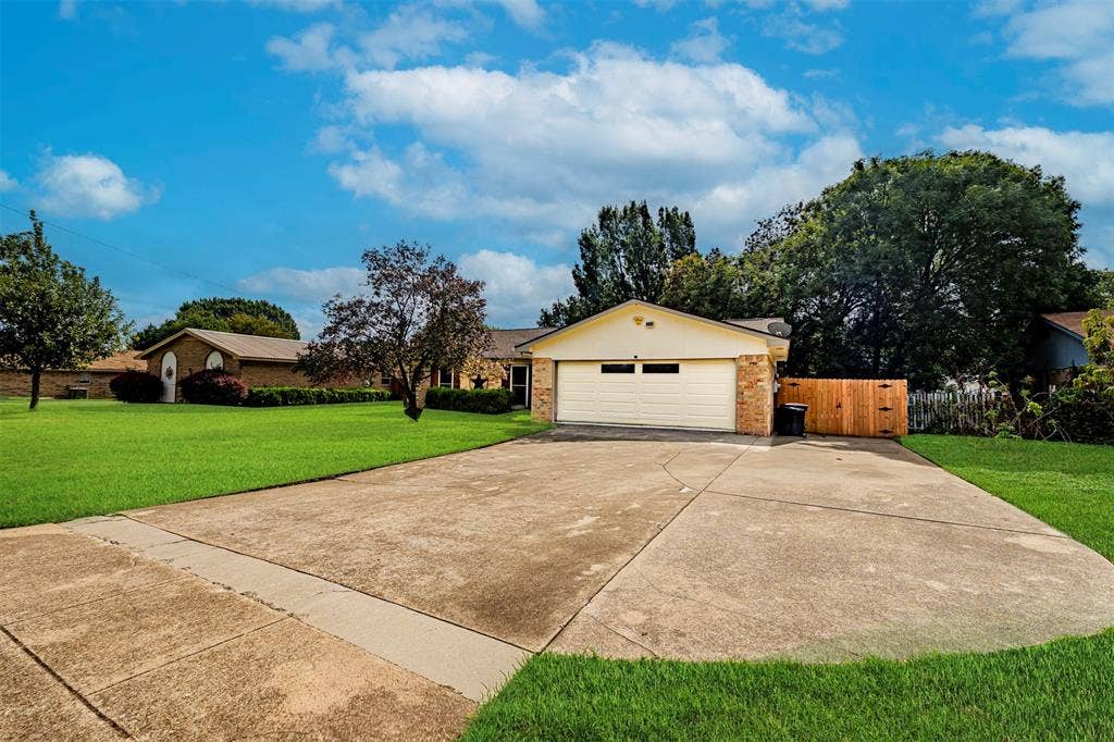 Exterior facade featuring a two-car garage, stone masonry accents, wood-style siding, an expansive driveway, and a wood privacy fence