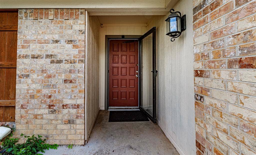 Covered entryway featuring a multi-panel door, textured brick exterior, vertical siding, and a decorative wall-mounted lantern light fixture
