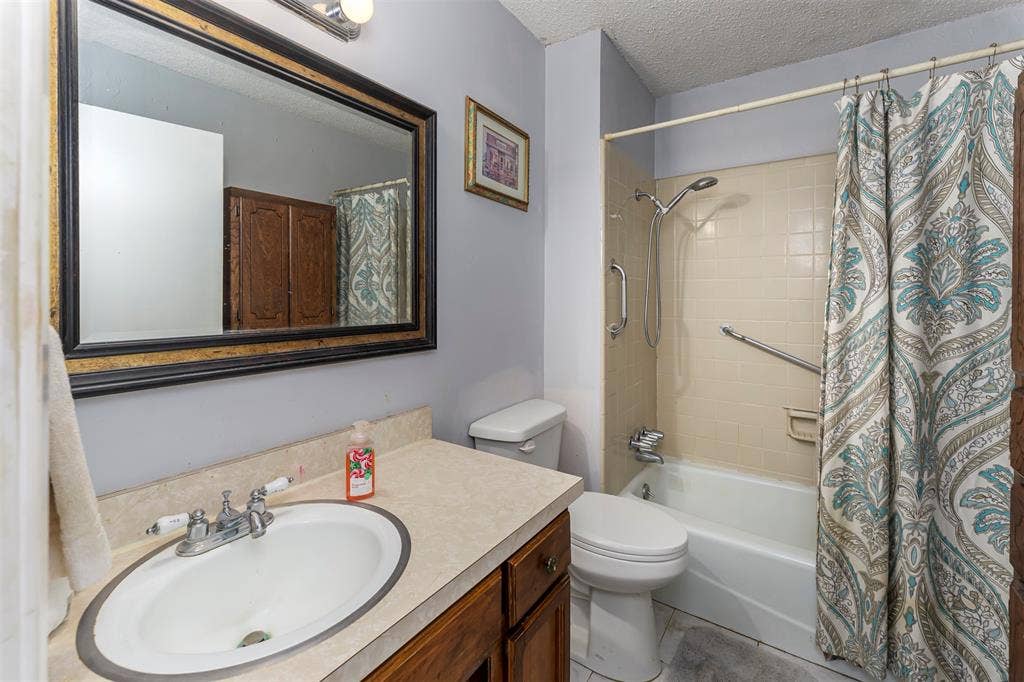 Bathroom featuring a wood vanity with a neutral countertop, an undermount sink, a framed wall mirror, and a tub-shower combination with ceramic tile surround