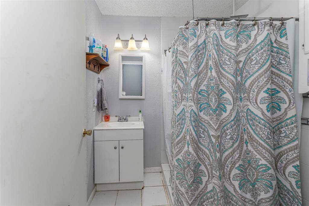 Bathroom featuring a white vanity cabinet with an integrated sink, three-light wall-mounted fixture, recessed medicine cabinet, and tiled flooring