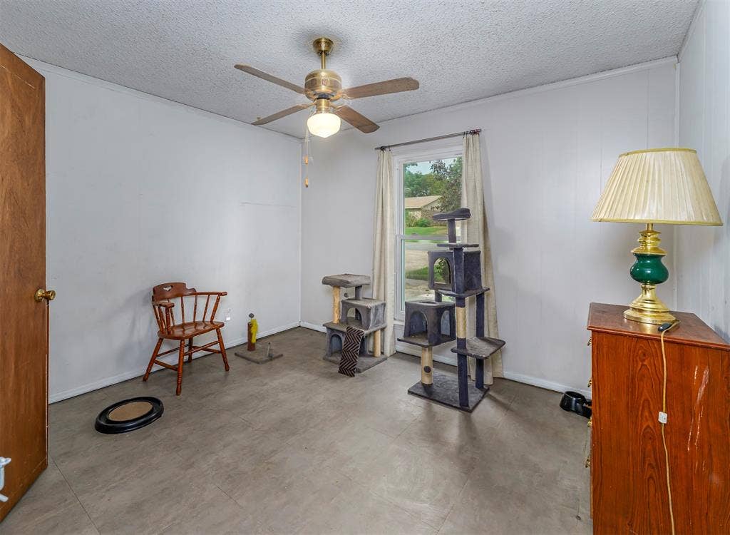 Room featuring a ceiling fan with integrated lighting, smooth-finish wall surfaces, neutral tile flooring, and a single-pane window