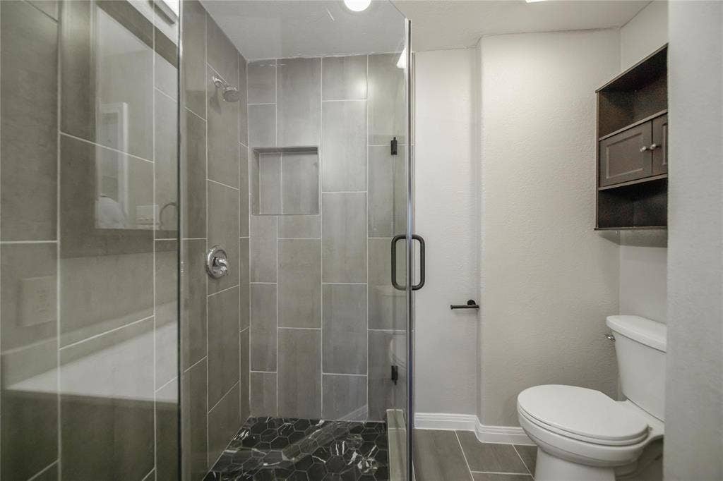 Walk-in shower with vertical tile surround, glass enclosure, recessed wall niche, and hexagonal floor tile, paired with built-in wall cabinetry