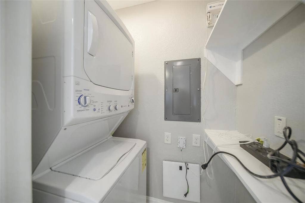 Utility room featuring a stacked washer and dryer, built-in shelving, and a wall-mounted electrical panel